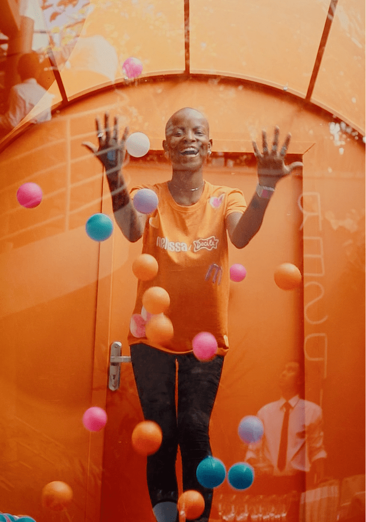Ativação de marca Melissa com participante sorrindo em cabine de bolinhas coloridas